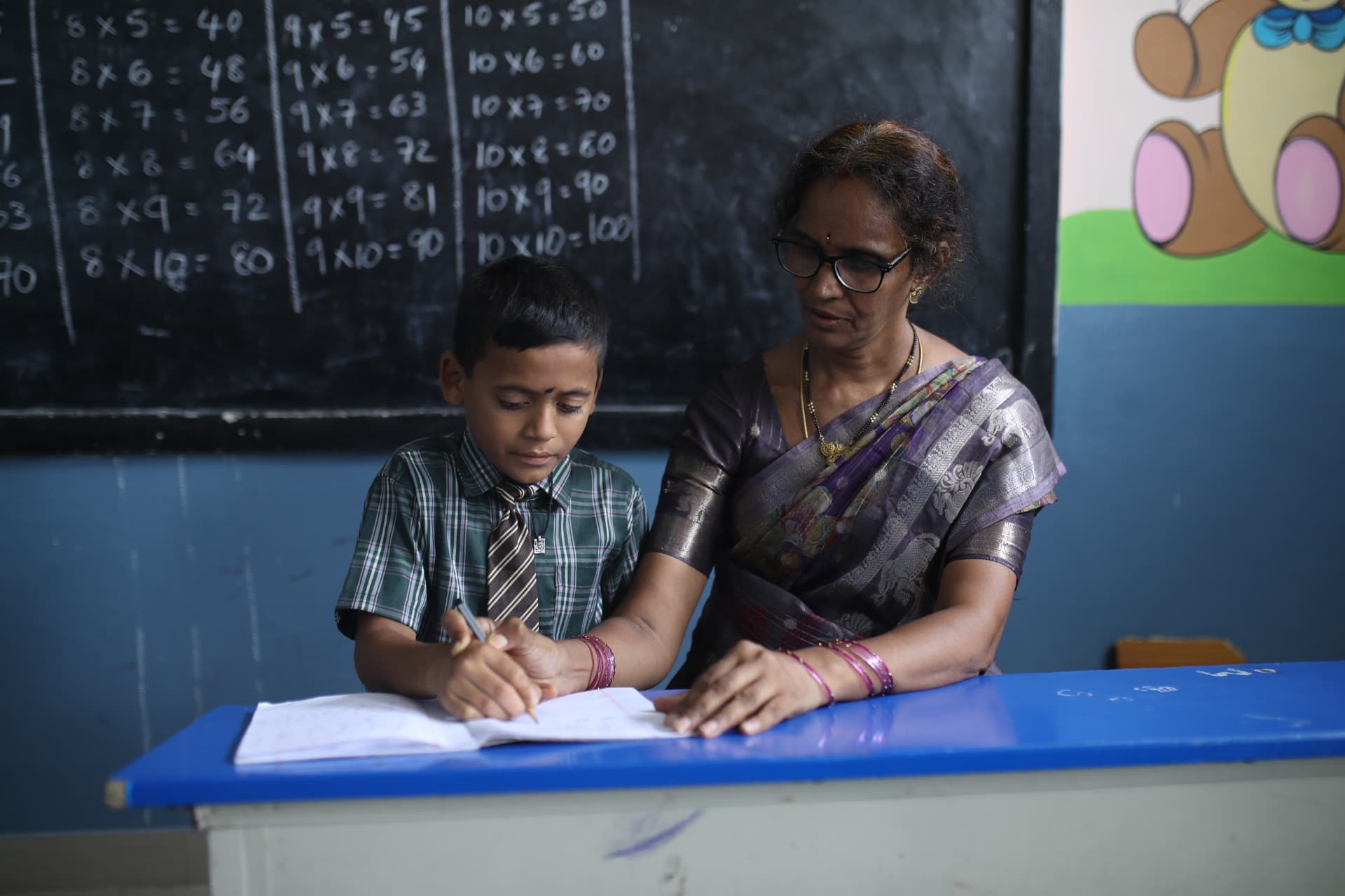 A teacher guiding an Aadarana student as he writes in his notebook