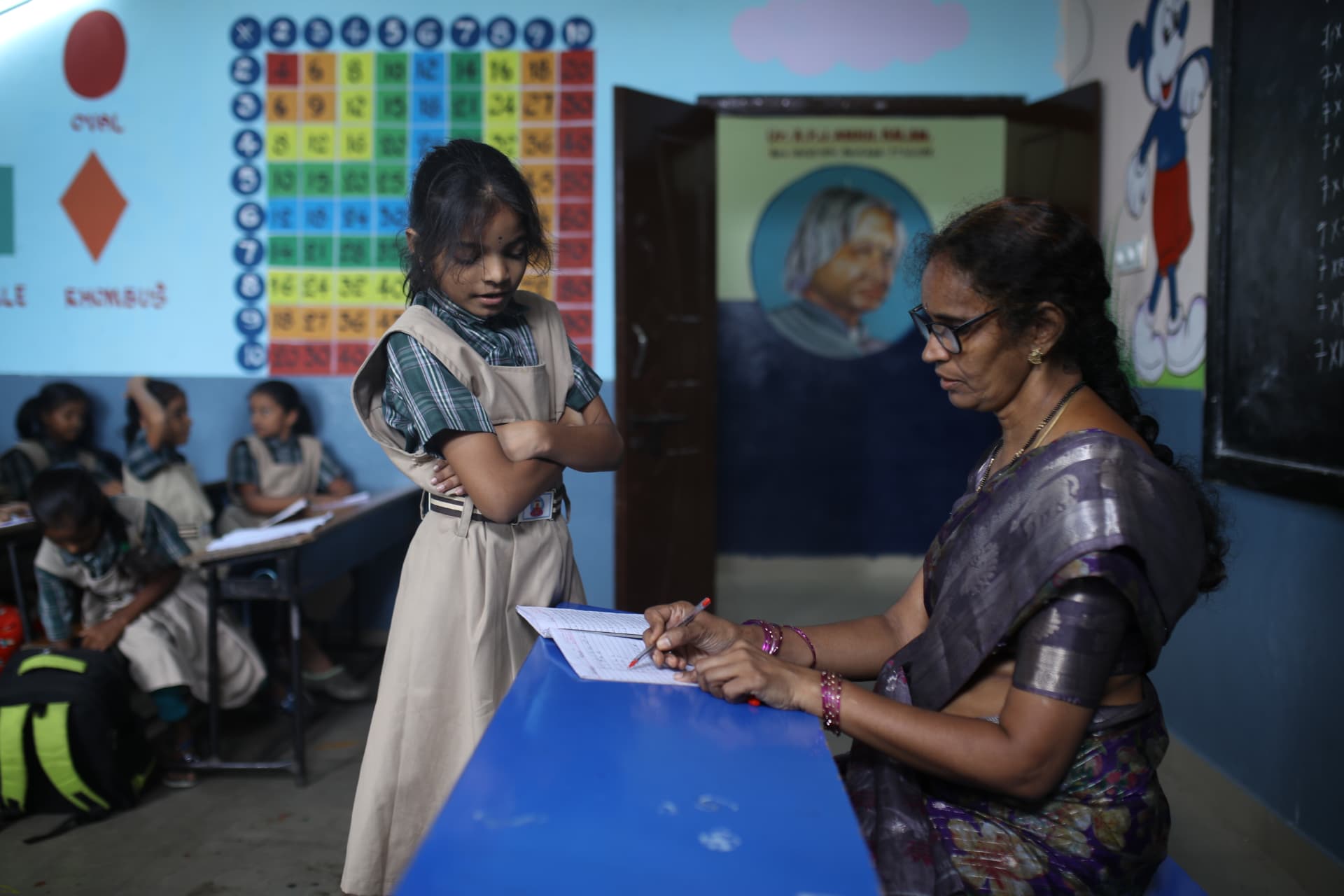 A teacher reviewing a schoolgirl’s written work at her desk