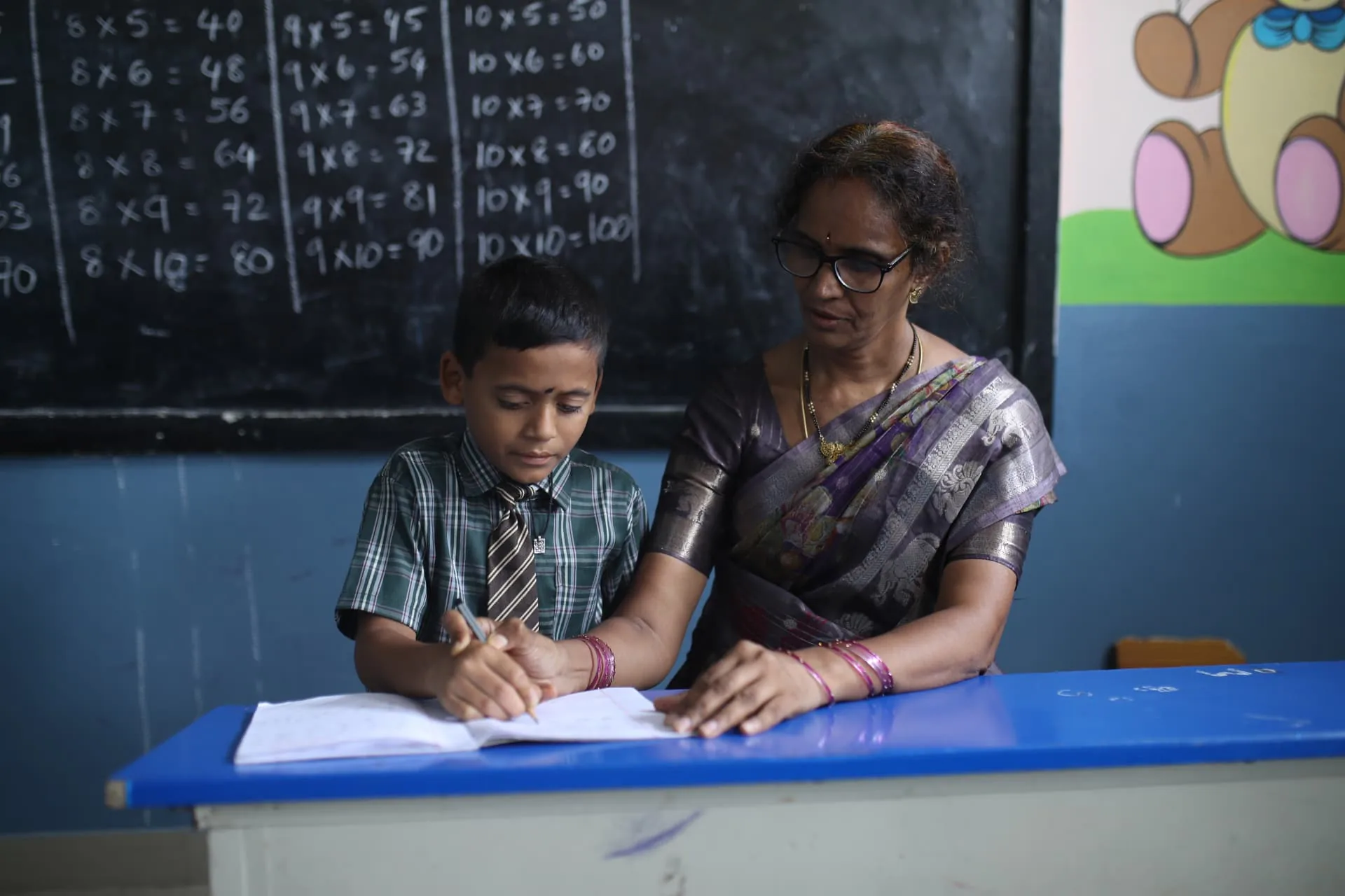 A teacher guiding an Aadarana student as he writes in his notebook